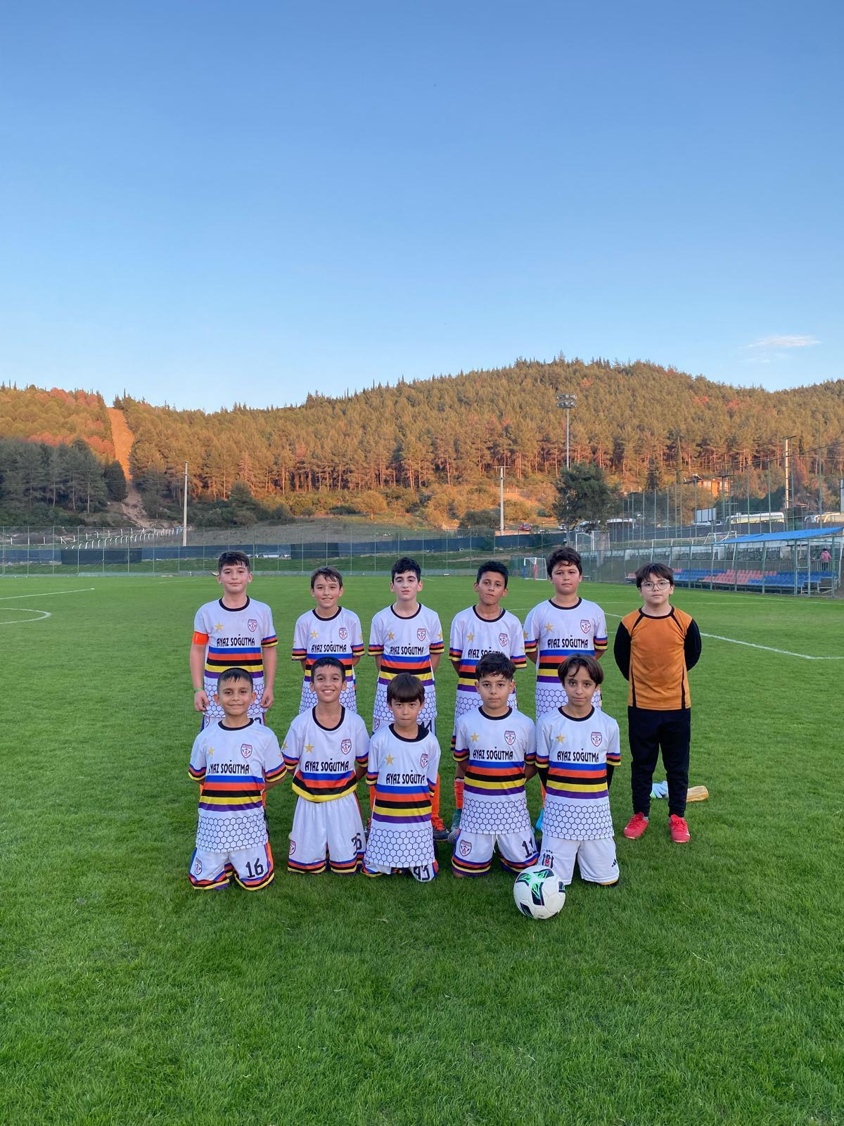 U11 2015 yaş grubu dağ manzaralı sahada beyaz forma takım pozu